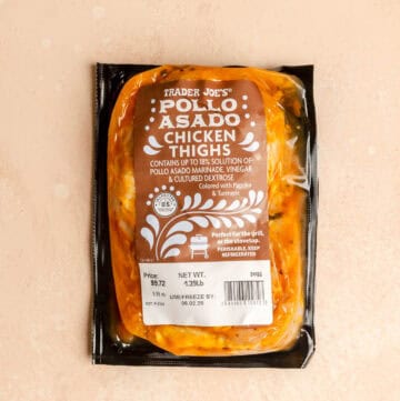 An unopened package of Trader Joe's Pollo Asado Chicken Thighs on a pink surface.