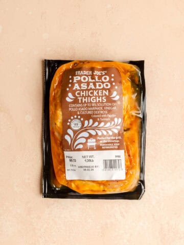 An unopened package of Trader Joe's Pollo Asado Chicken Thighs on a pink surface.