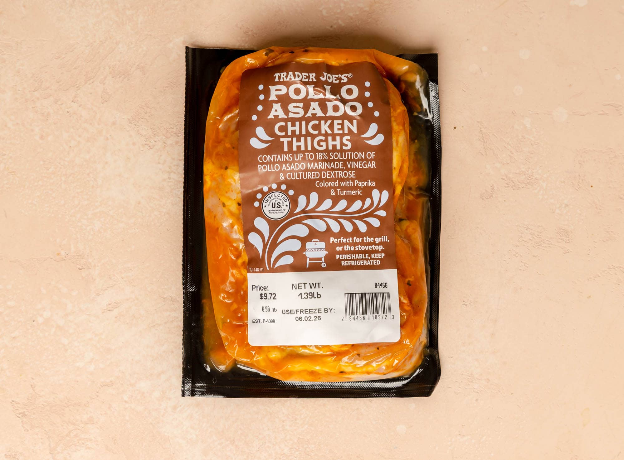 An unopened package of Trader Joe's Pollo Asado Chicken Thighs on a pink surface.