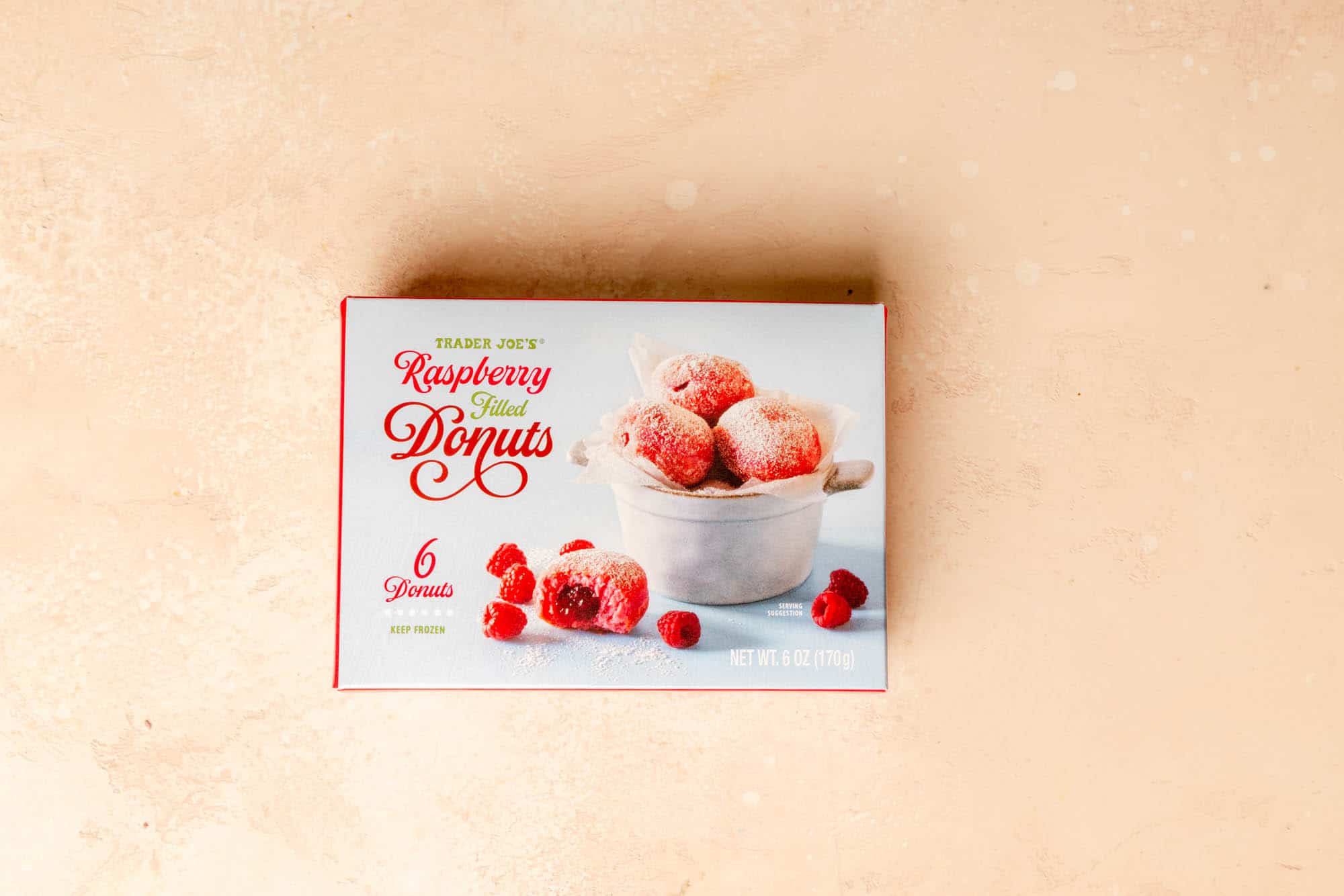 An unopened box of Trader Joe's Raspberry Filled Donuts on a pink surface.
