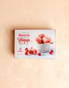 An unopened box of Trader Joe's Raspberry Filled Donuts on a pink surface.