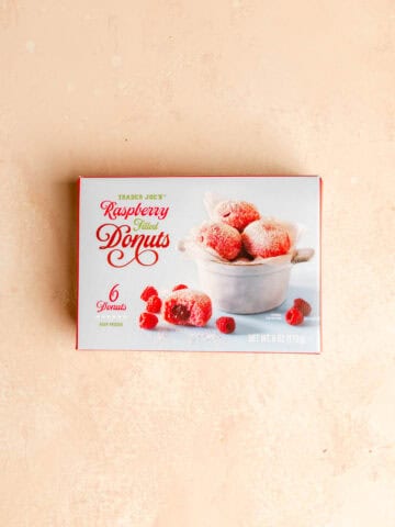 An unopened box of Trader Joe's Raspberry Filled Donuts on a pink surface.