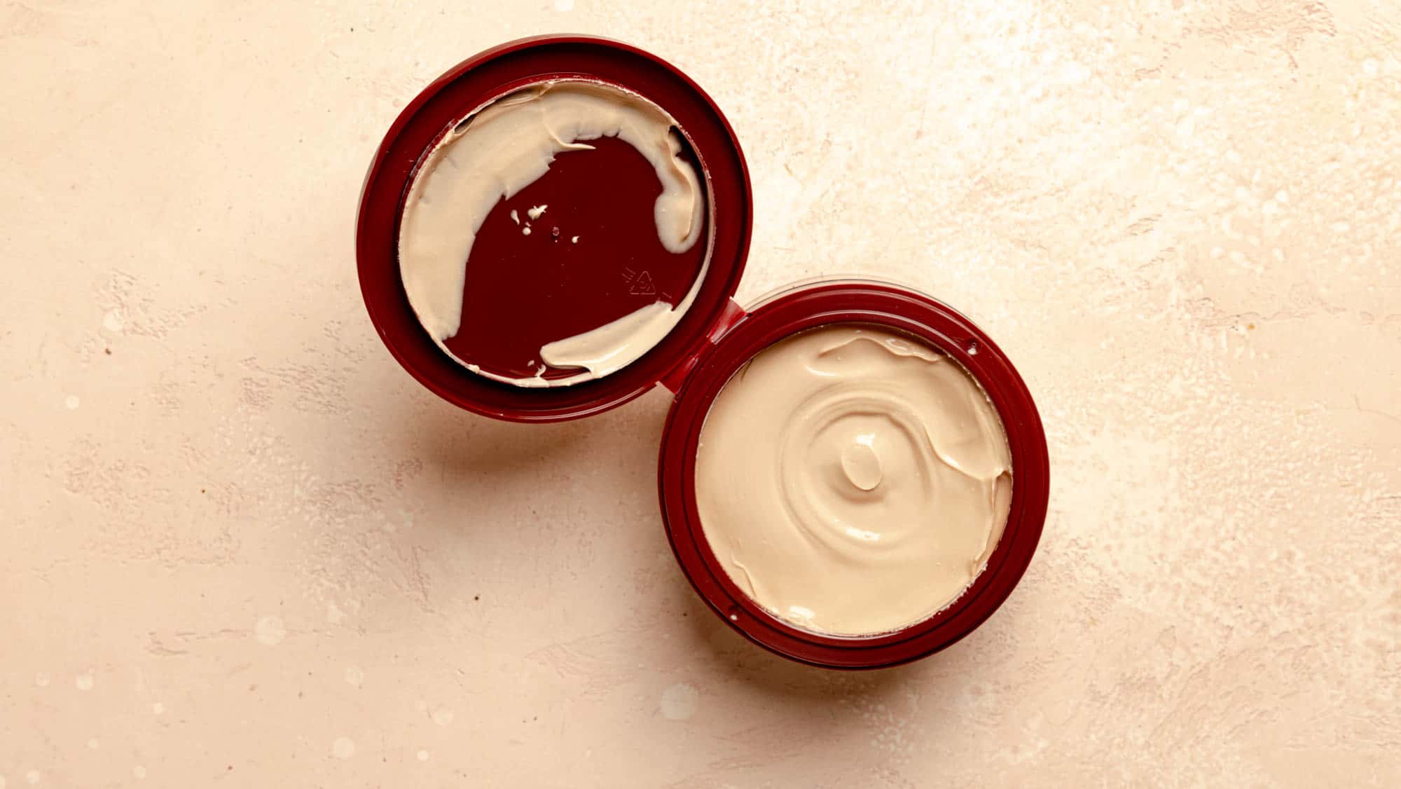 An open package of Trader Joe's Caramel Creme Body Butter on a pink surface.