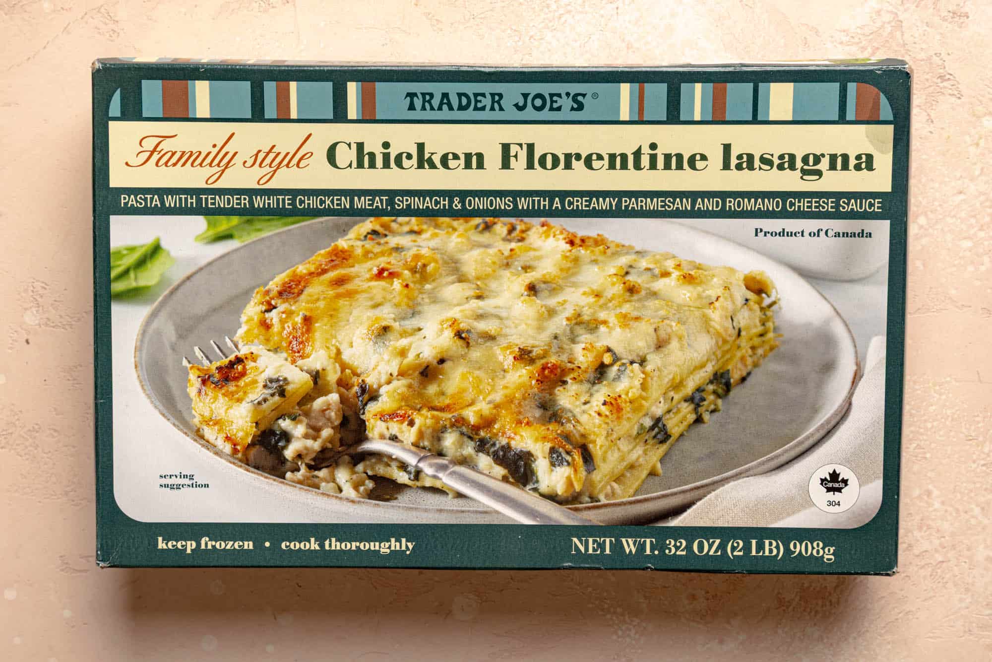 An unopened package of Trader Joe's Family Style Chicken Florentine Lasagna on a pink surface.