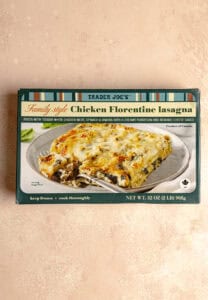 An unopened box of Trader Joe's Family Style Chicken Florentine Lasagna on a pink surface.