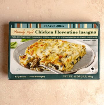 An unopened box of Trader Joe's Family Style Chicken Florentine Lasagna on a pink surface.