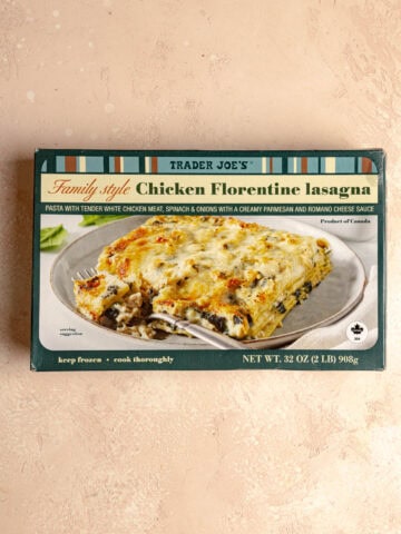 An unopened box of Trader Joe's Family Style Chicken Florentine Lasagna on a pink surface.